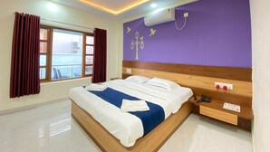 Una habitación de hotel moderna con una cama grande, cabecera de madera, mesita de noche, ventana con cortinas y ventilador de techo.
