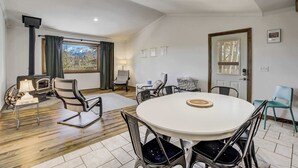 A modern living room with a round dining table, comfortable seating, a fireplace, and a large window offering a mountain view.