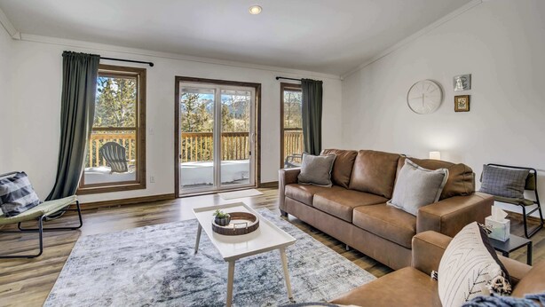 A living room with a brown leather sofa, a white coffee table, and a view of a wooden deck through large windows.