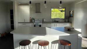 Eine moderne Küche mit Kochinsel, Barhocker, Pendelleuchten und Blick auf Grünflächen.