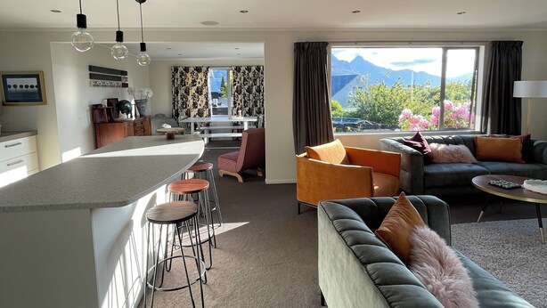 Ein modernes Wohnzimmer mit einer großen Couch, einem Essbereich mit Bar und Bergblick durch große Fenster.
