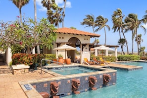 A resort pool area with palm trees, lounge chairs, and a building with a tiled roof.