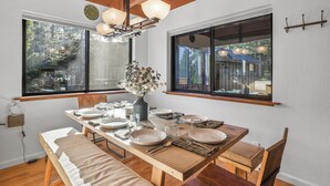 A dining area with a wooden table set for four, large windows, and a ceiling with exposed beams.