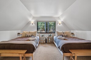 Un dormitorio con dos camas, una ventana que da a árboles y una mesita entre las camas.