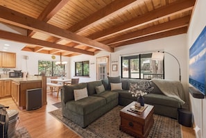 A spacious living area with a wooden ceiling, a sectional sofa, a coffee table, and a large window.