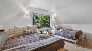 A bedroom with two beds, a window, and a view of greenery outside.