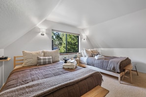 A bedroom with two beds, a window, and a view of greenery outside.