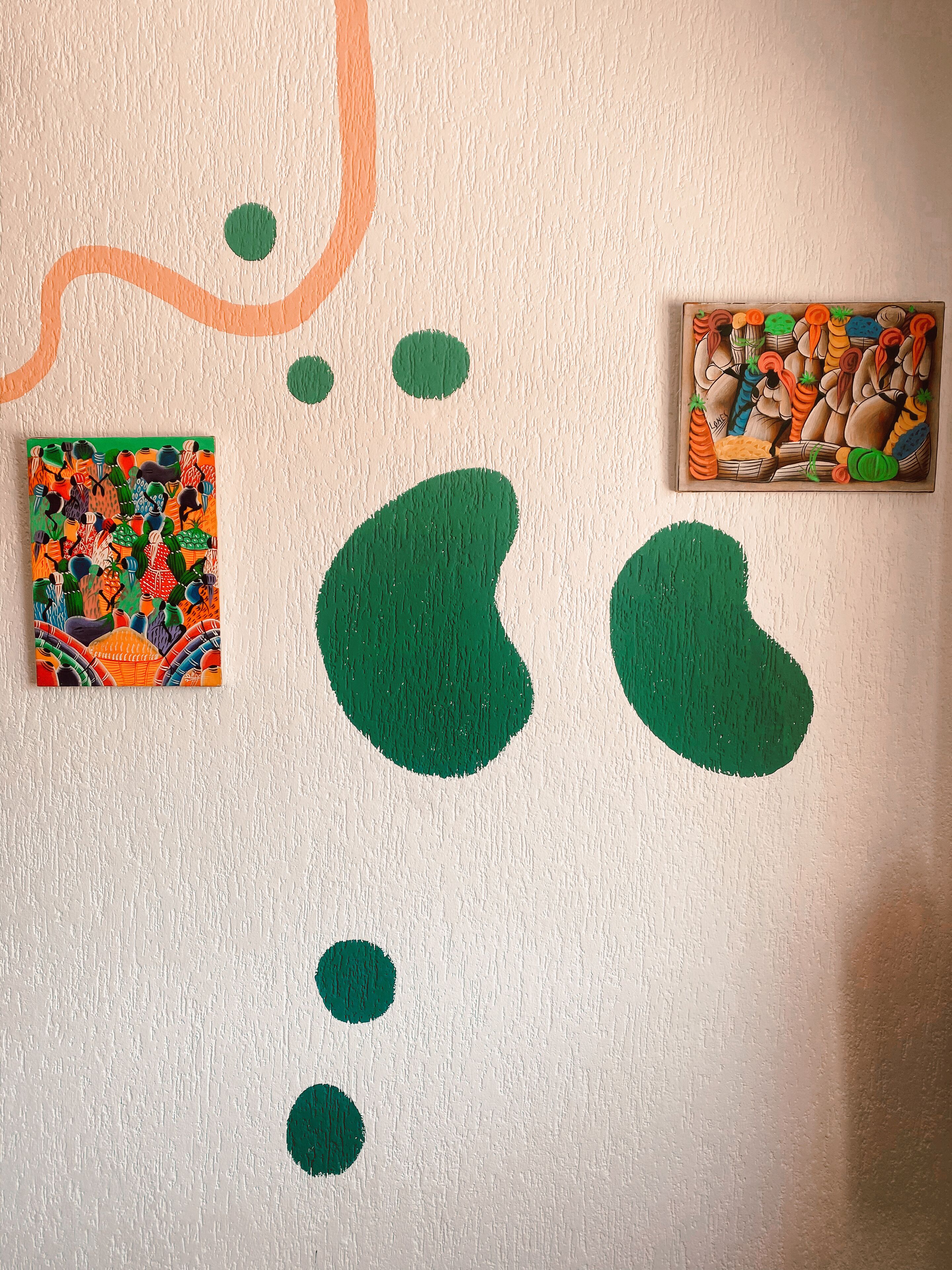 A wall with two paintings and abstract green shapes.