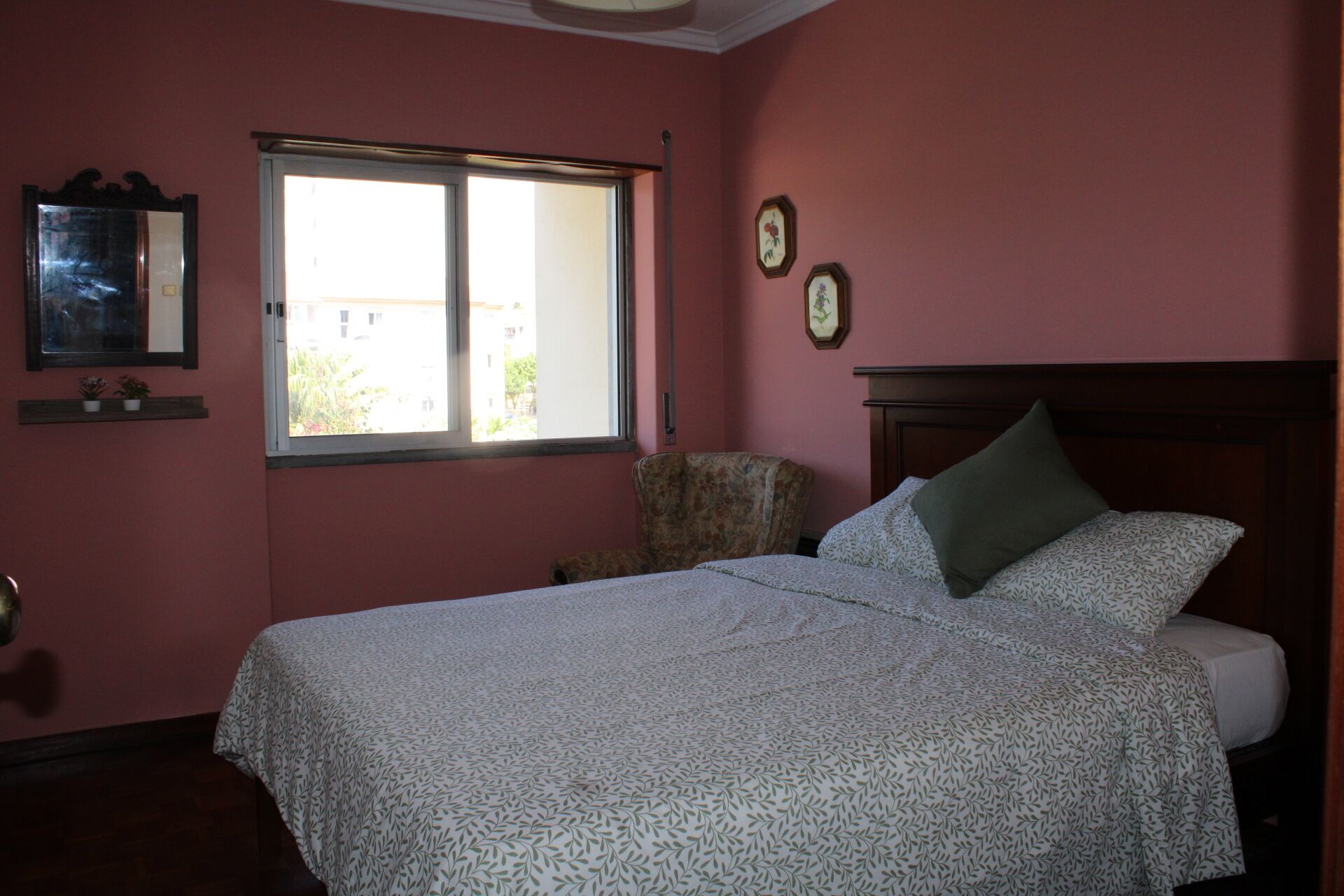 Un dormitorio con una cama, una silla, un ventanal y una pared decorada con dos cuadros.