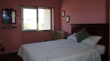 Un dormitorio con una cama, una silla, un ventanal y una pared decorada con dos cuadros.