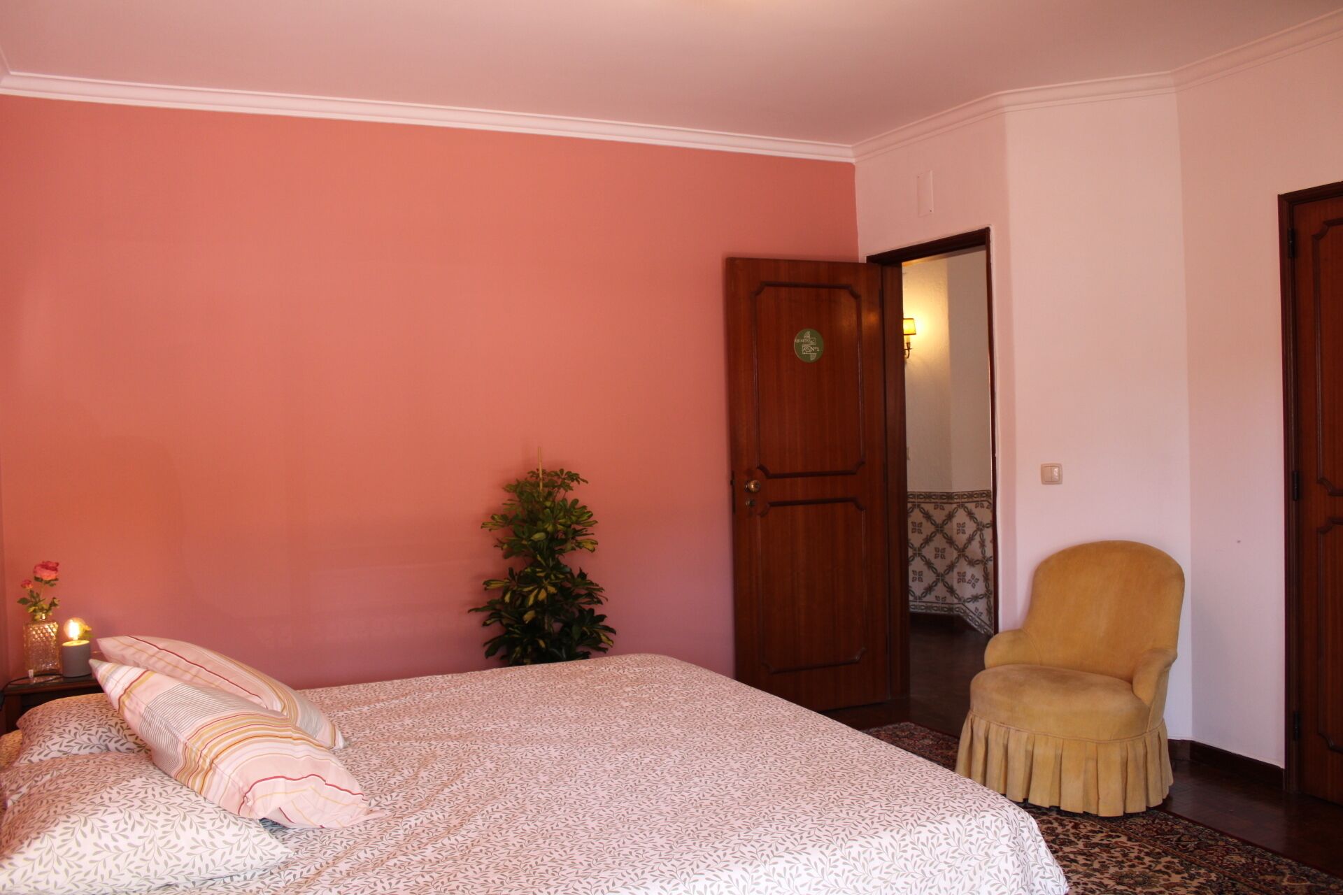 A bedroom with a bed, a chair, a door, and a plant.