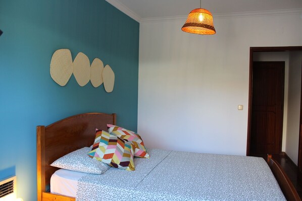 A bedroom with a wooden bed, patterned bedding, a wall decoration, and a hanging light fixture. - Villa do Sol (Cascais)