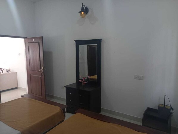 A bedroom with a bed, a dresser, a mirror, and a wall-mounted light fixture. - RAJABAWANA Holiday Resort (Anuradhaura)