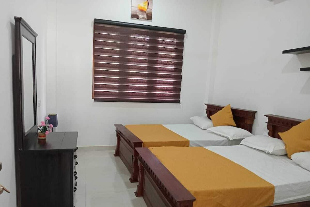 A hotel room with two single beds, a wooden dresser, a mirror, and a window with blinds.