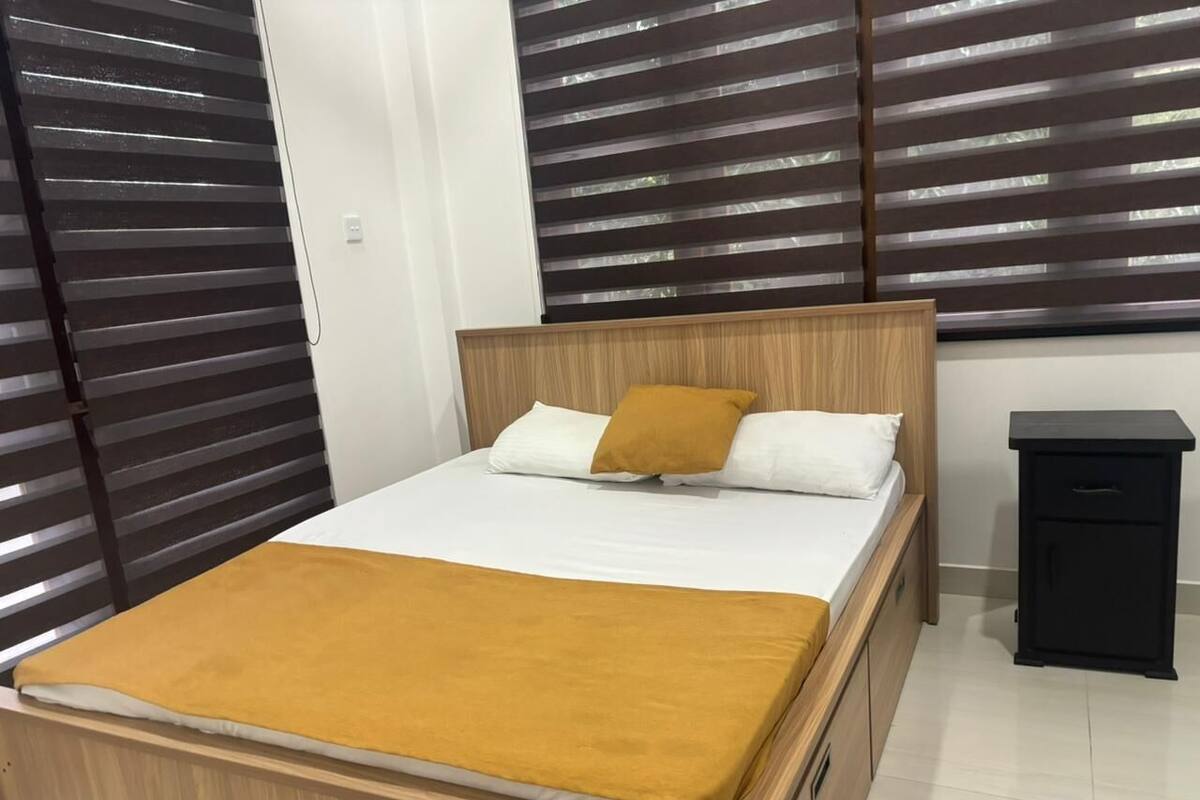 A bed with a wooden frame, white bedding, and a mustard-colored throw blanket.