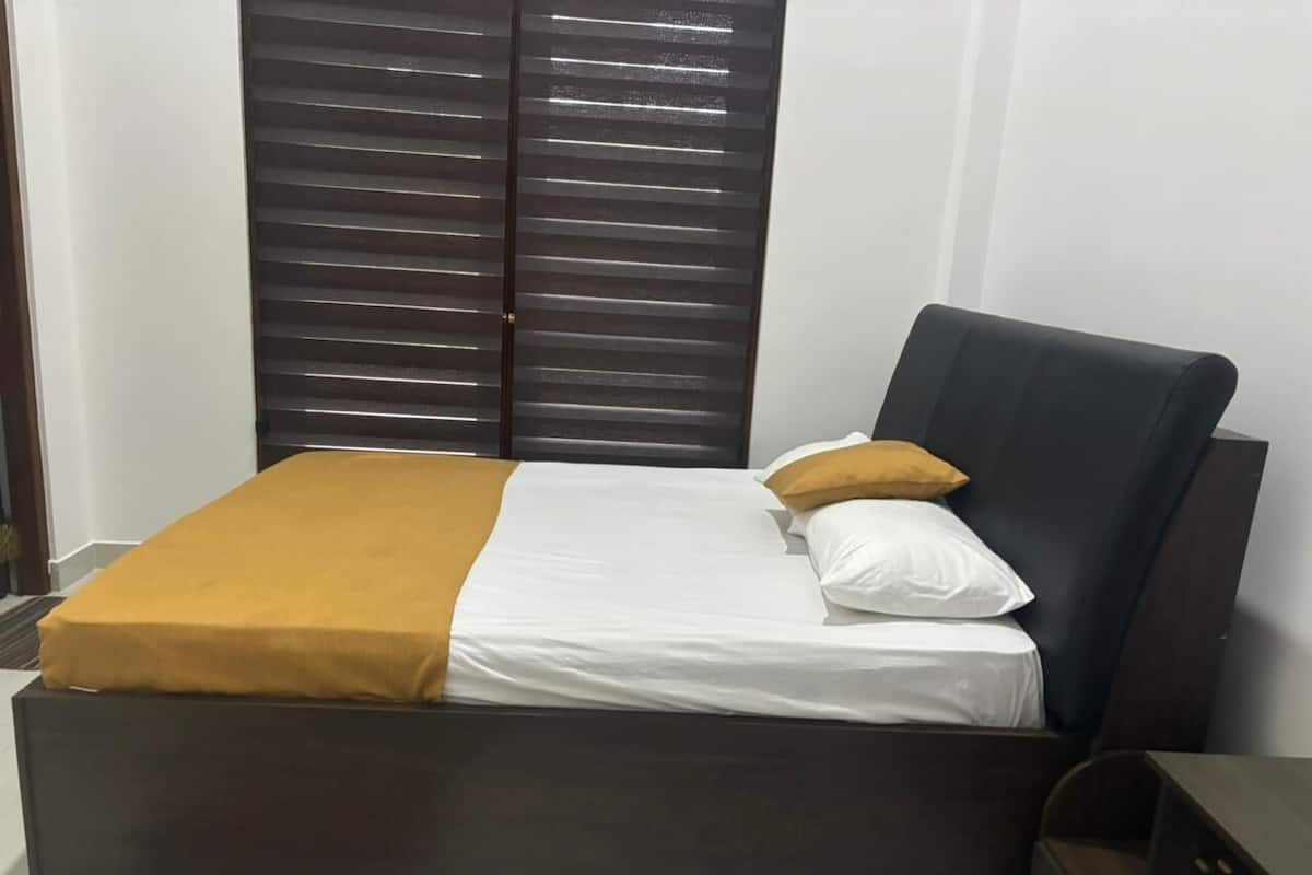 A bed with a dark headboard, white bedding, and a mustard-colored throw blanket.
