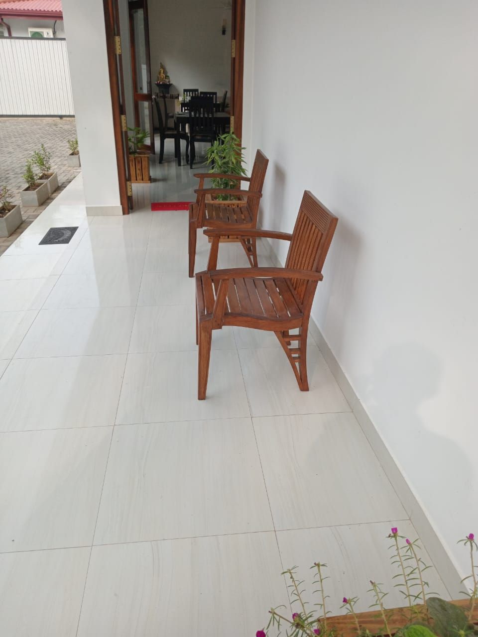 A patio area with two wooden chairs and a table, a tiled floor, and a potted plant.