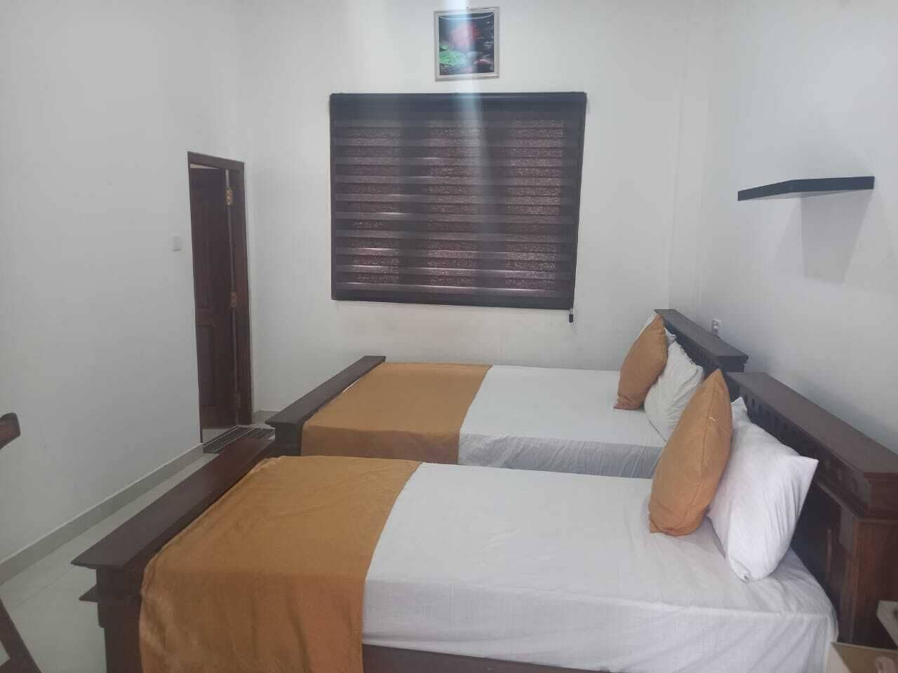 A hotel room with two beds, each with a wooden headboard and white bedding. There is a window with a view of the outside, and a small shelf above the beds.