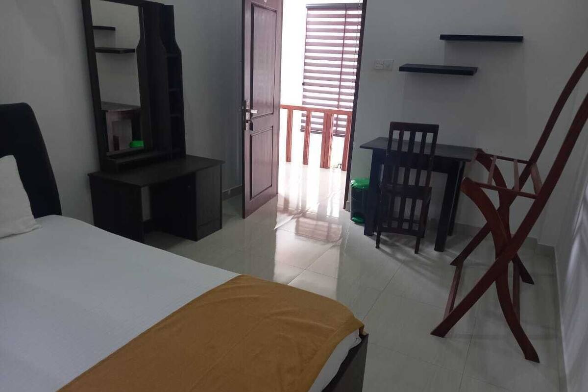 A hotel room with a bed, a desk, and a chair. There is a door leading to a balcony with a view.