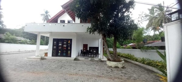 Un edificio moderno con acceso cubierto, una zona de estar con mesas y sillas, y un camino de entrada pavimentado.