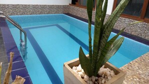 Ein Schwimmbecken mit Metallleiter, umrahmt von einem Kiesstreifen und einem Blumentopf mit weißen Kieselsteinen.