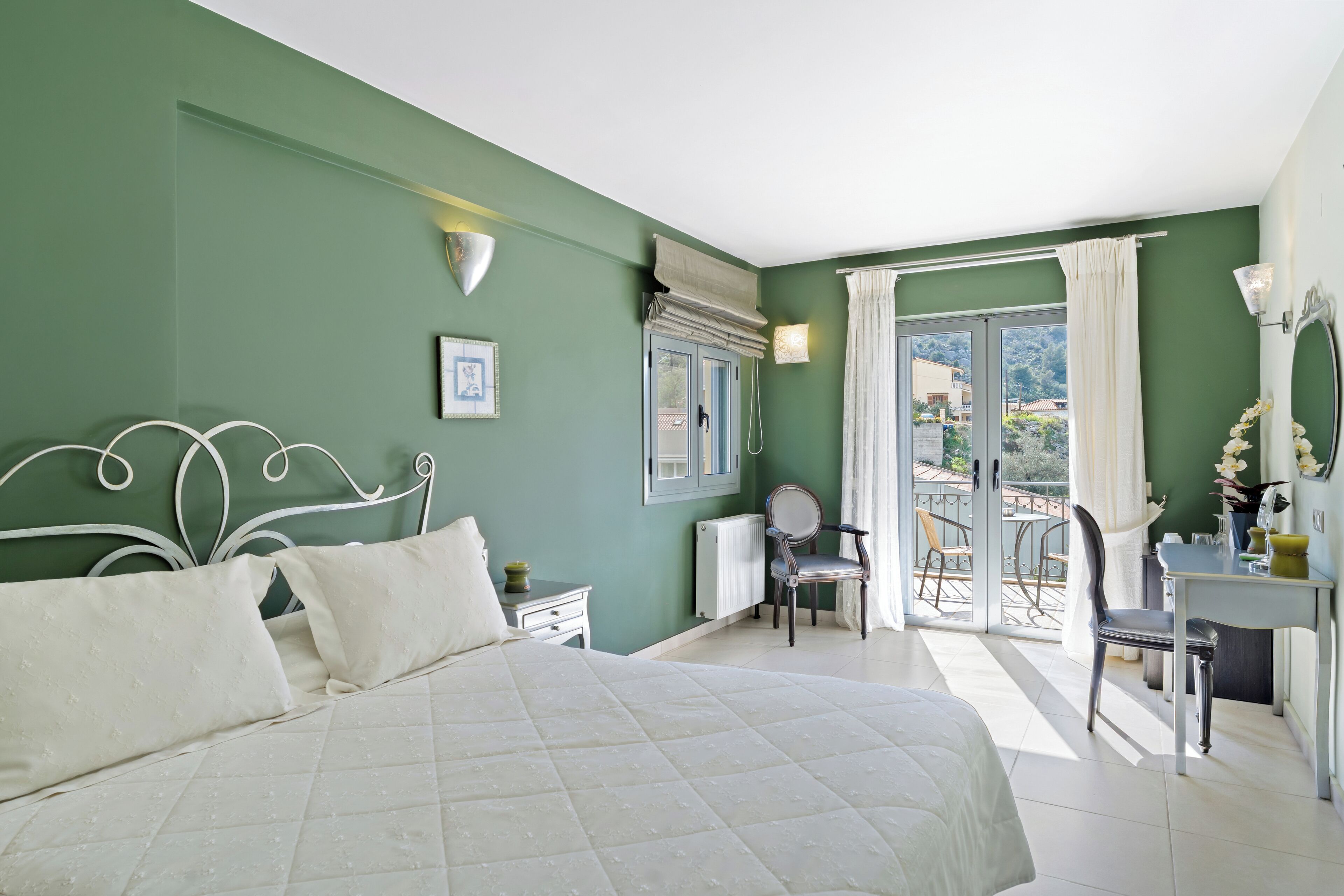 Ein Schlafzimmer mit einem Bett, einem Schreibtisch und einem Stuhl. Ein Fenster mit Vorhängen bietet einen Ausblick ins Freie.