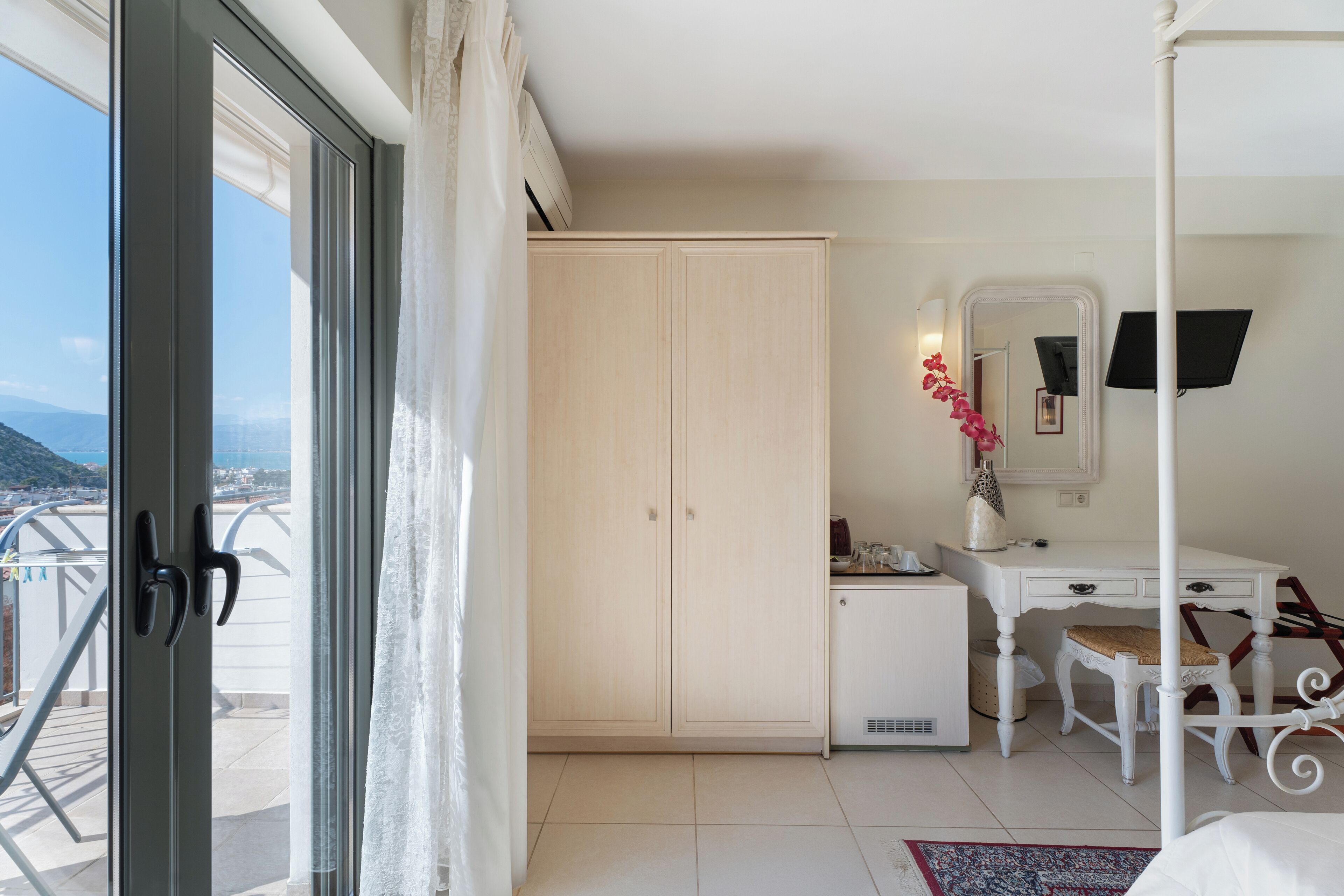 A room with a large wardrobe, a desk with a chair, a small cabinet, and a mirror.