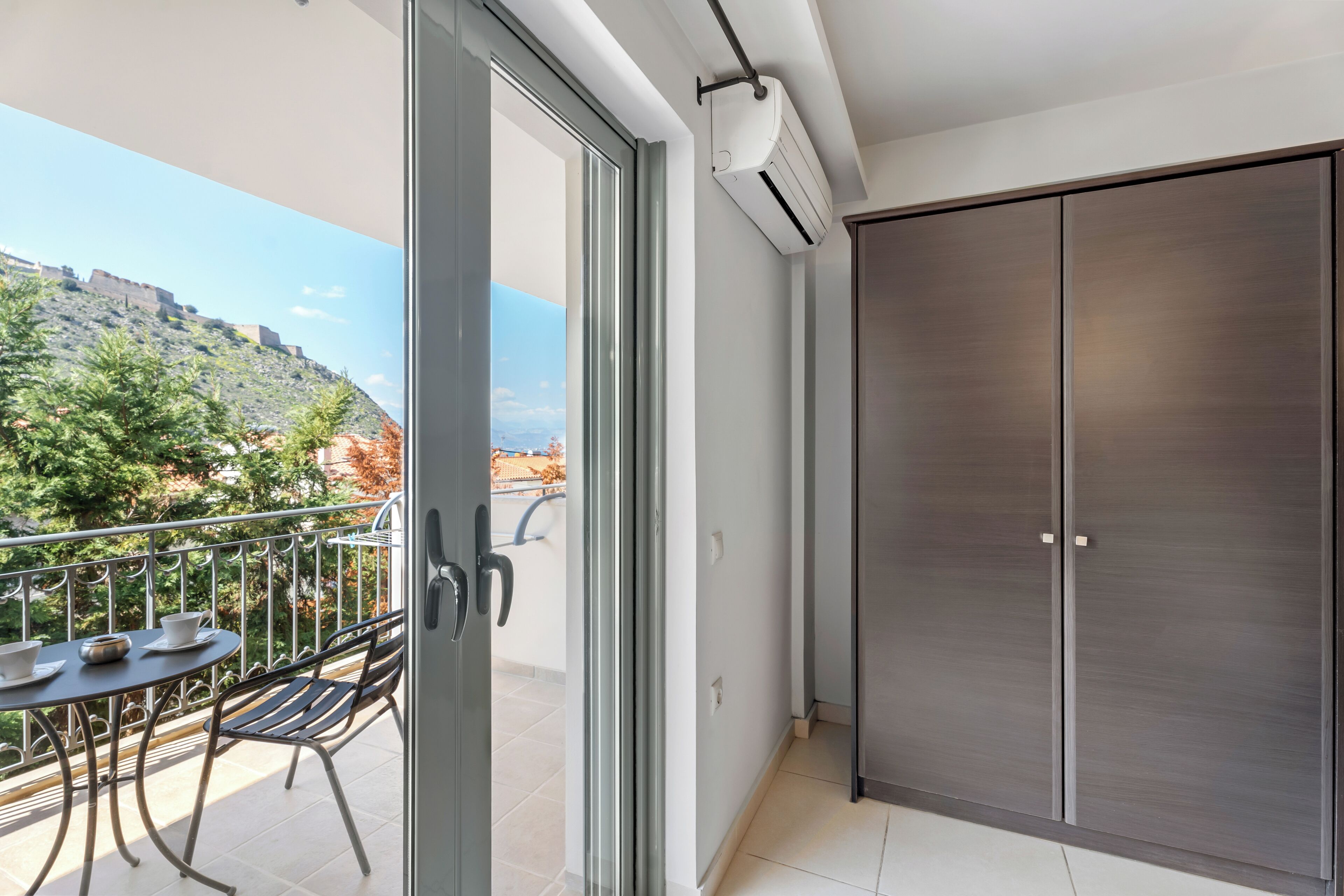 Ein Balkon mit Tisch und Stühlen, eine Schiebetür und Blick auf eine Hügelkuppe.