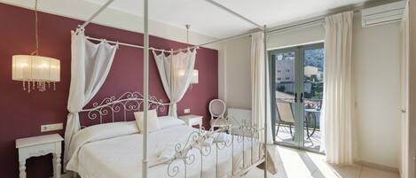 Uma cama de dossel com cortina, uma mesinha de cabeceira, uma cadeira e vista para o exterior.