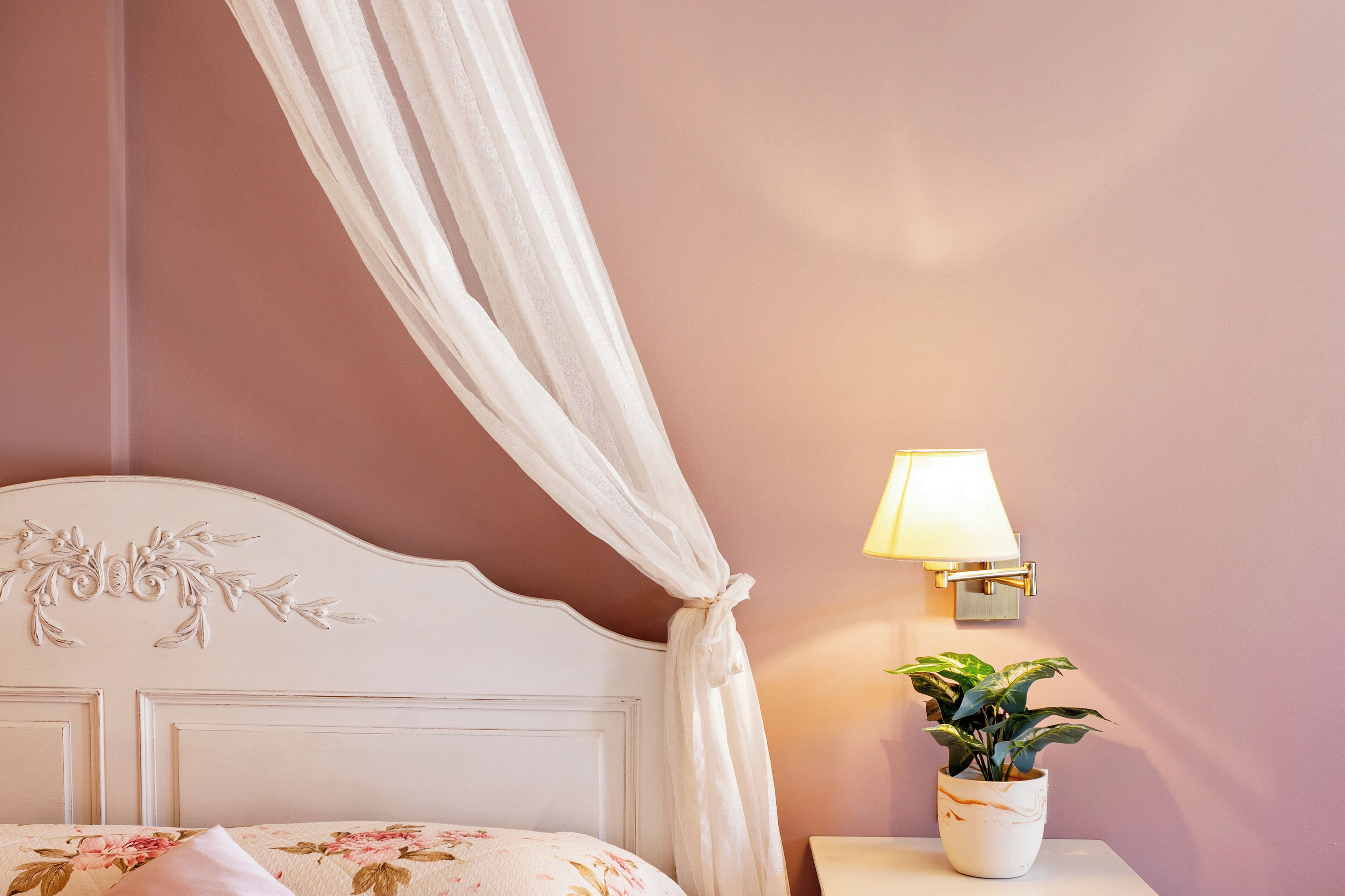 A bedroom with a bed, a nightstand with a lamp, and a potted plant.