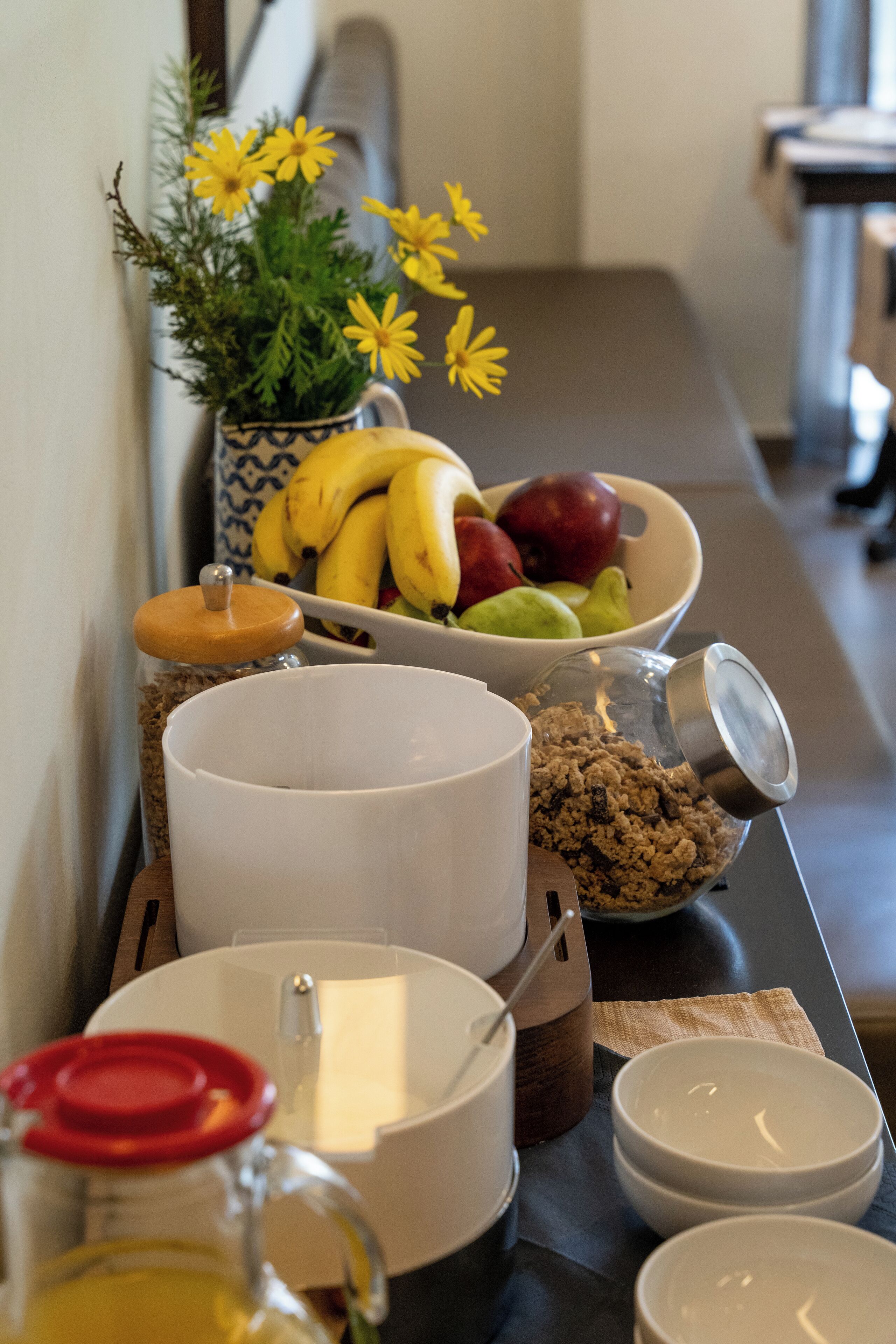 A breakfast setup with a bowl of fruit, a jar of jam, a pitcher of juice, and a coffee pot on a table.