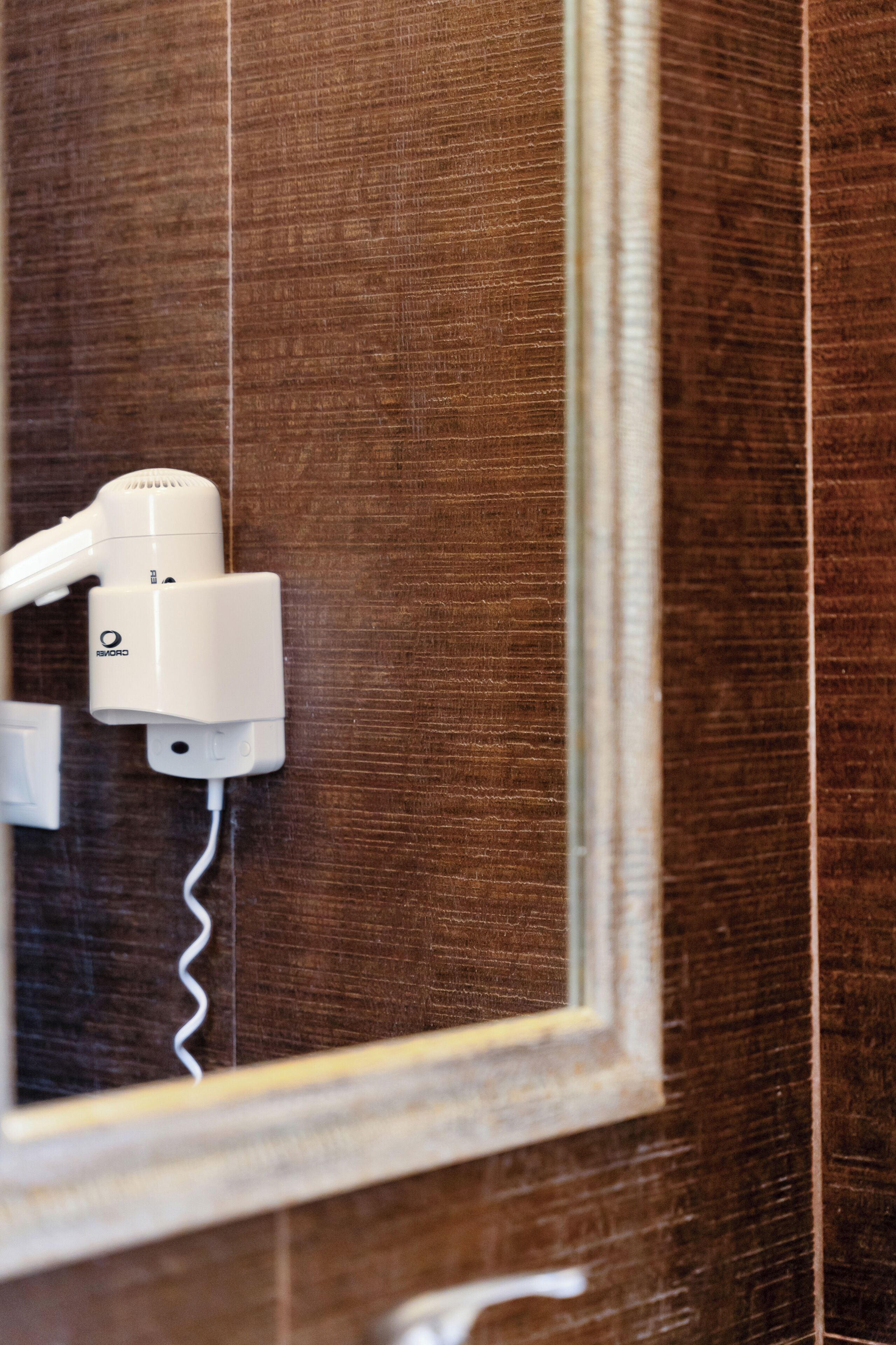 A hairdryer mounted on a wall with a mirror reflecting the wall.