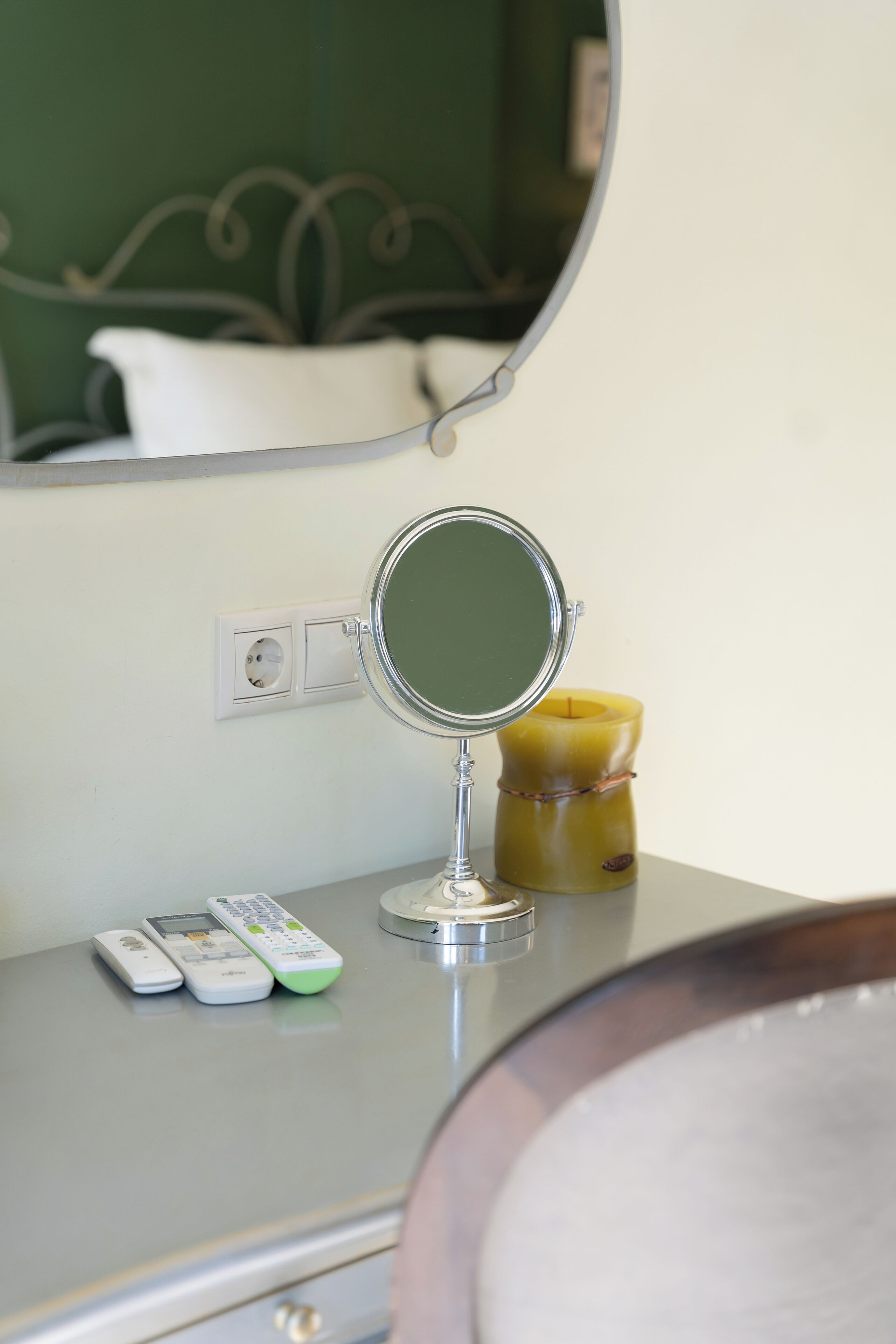 A bathroom vanity with a round mirror, a yellow candle, and a remote control.