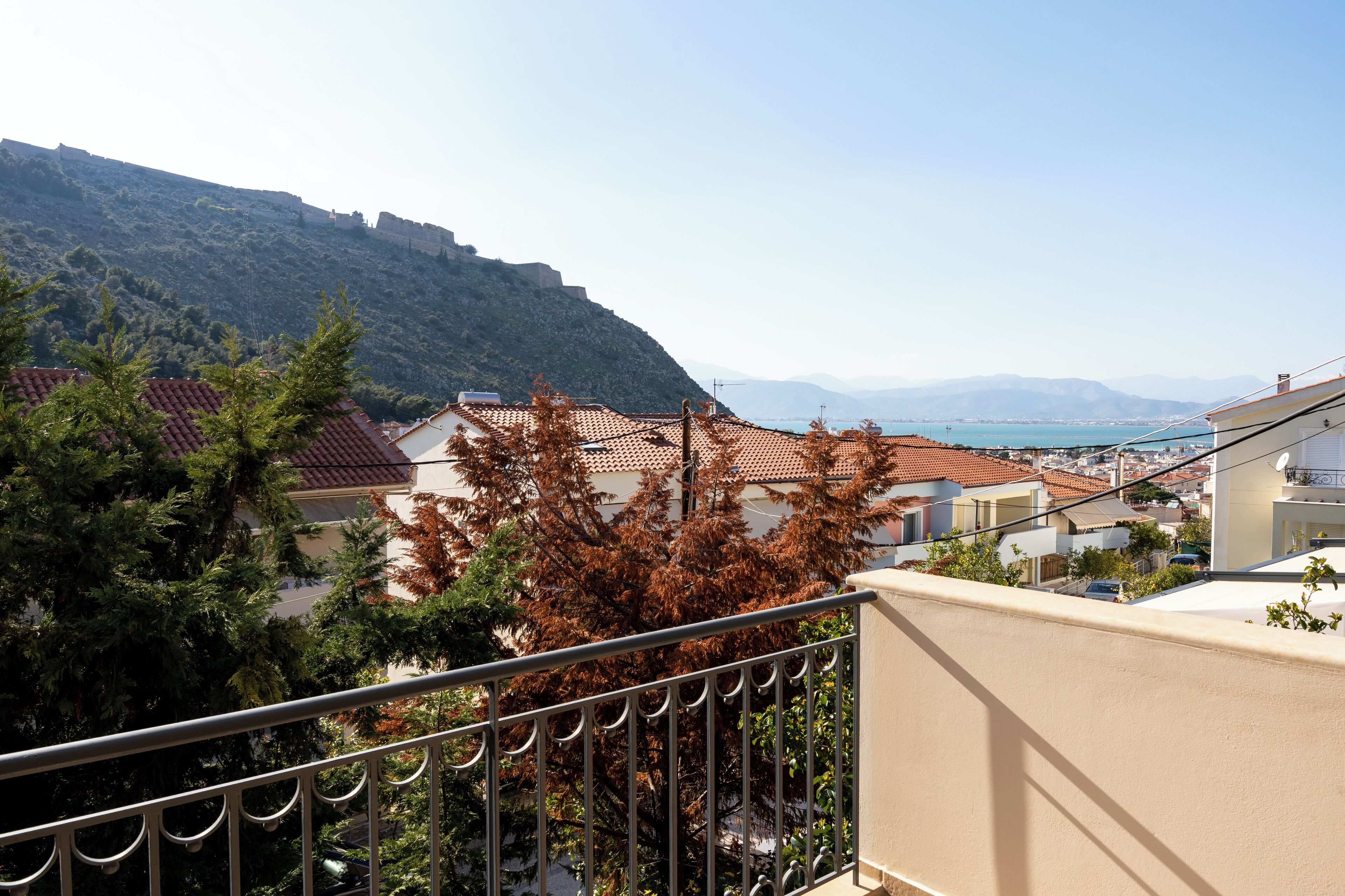 A coastal town with terracotta-roofed buildings, a hill with a fortification, and a clear view of the sea.