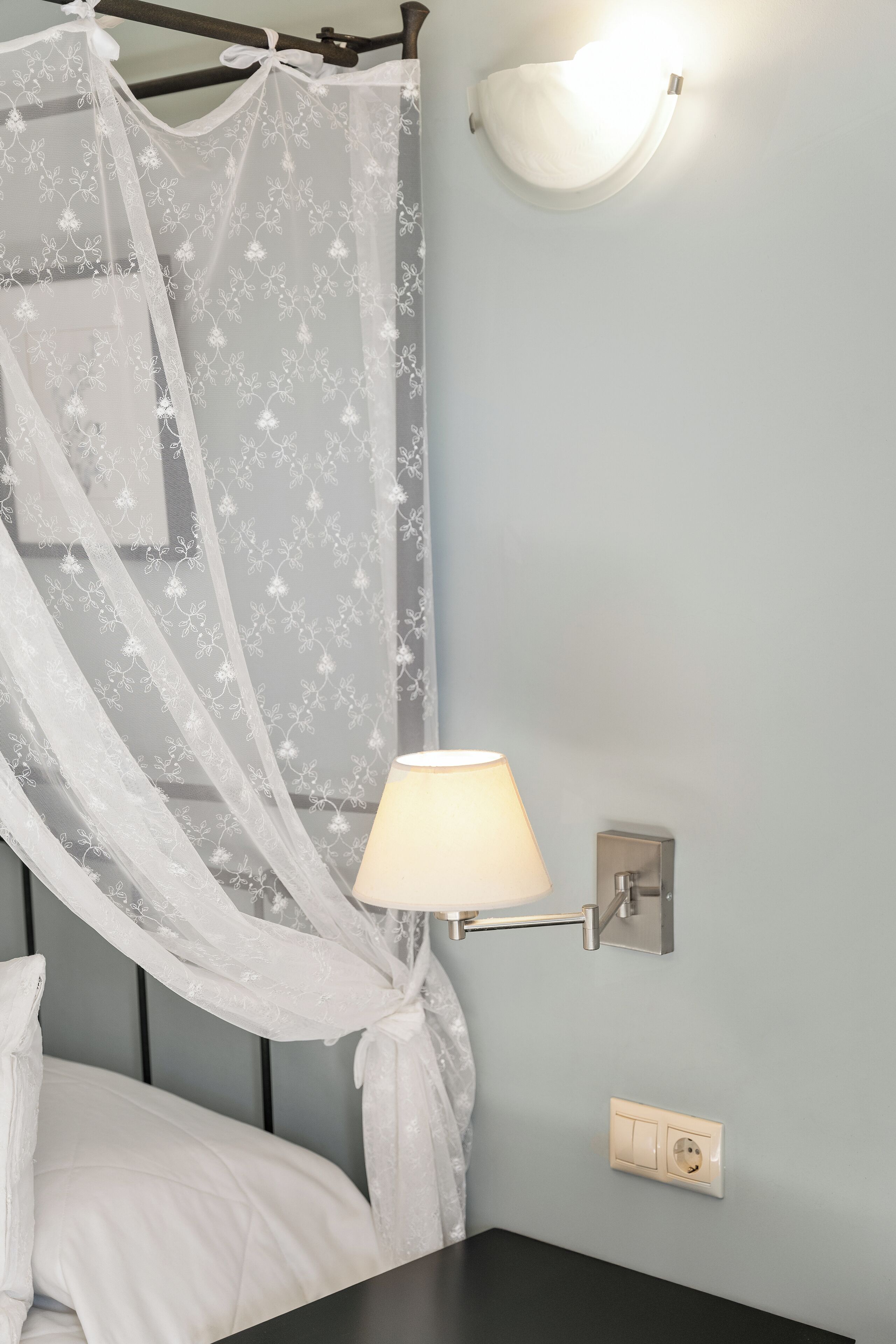 Une chambre à coucher comprenant un lit, une table de chevet, une lampe fixée au mur et une prise de courant.