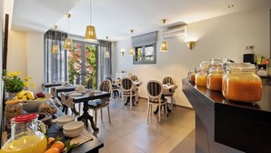 Un'area pranzo moderna con diversi tavoli e sedie, un bancone cucina con generi alimentari e ampie finestre con tende.