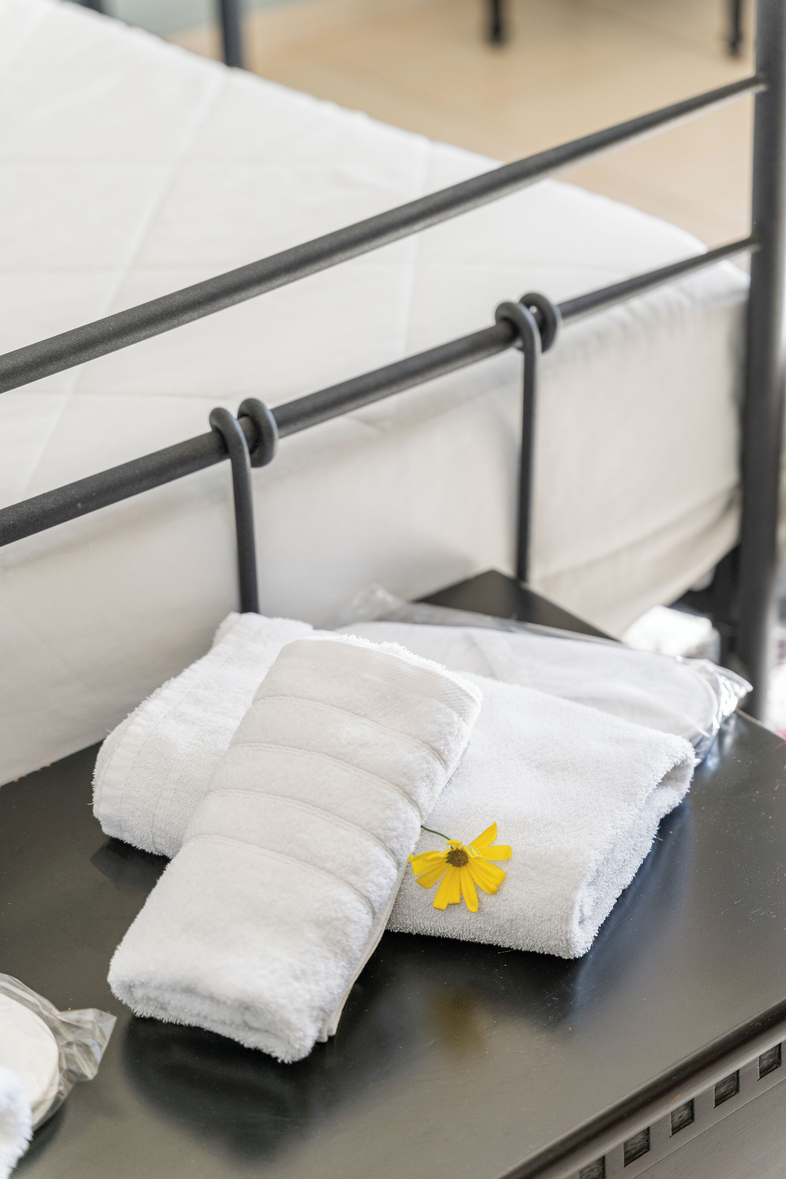 Una cama bien hecha con sábanas blancas y una flor amarilla.