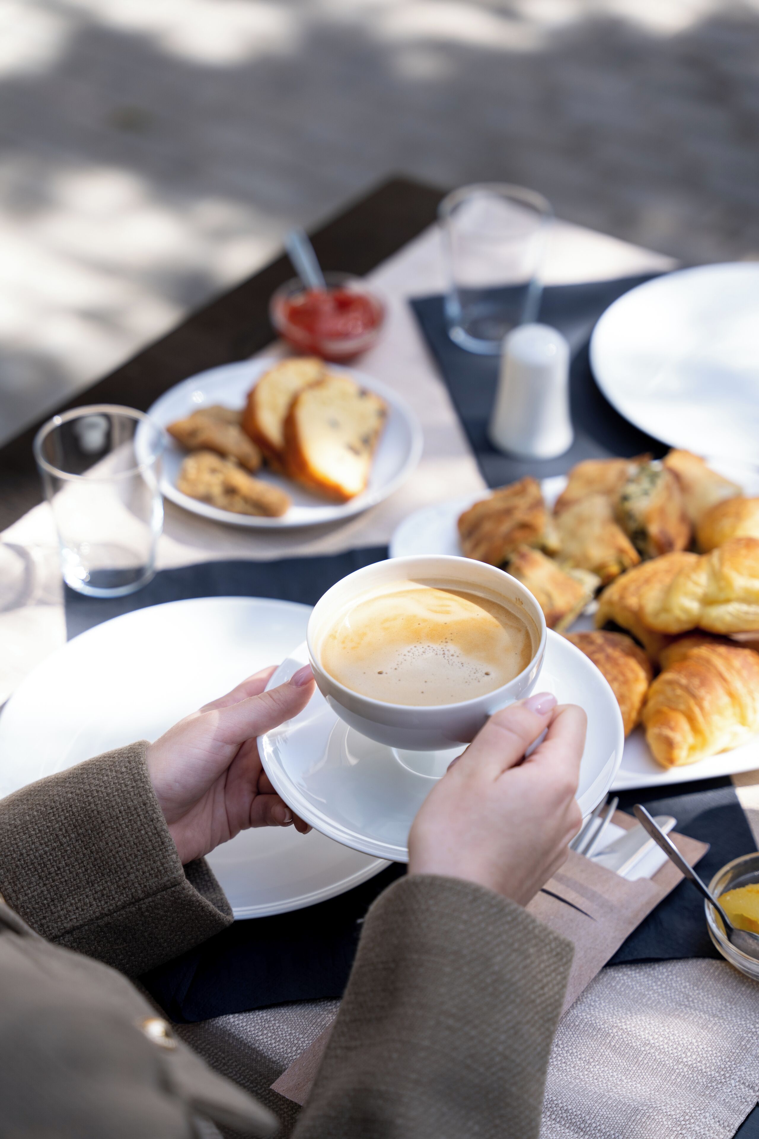 A person holding a cup of coffee with a plate of croissants and a glass of water on a table.