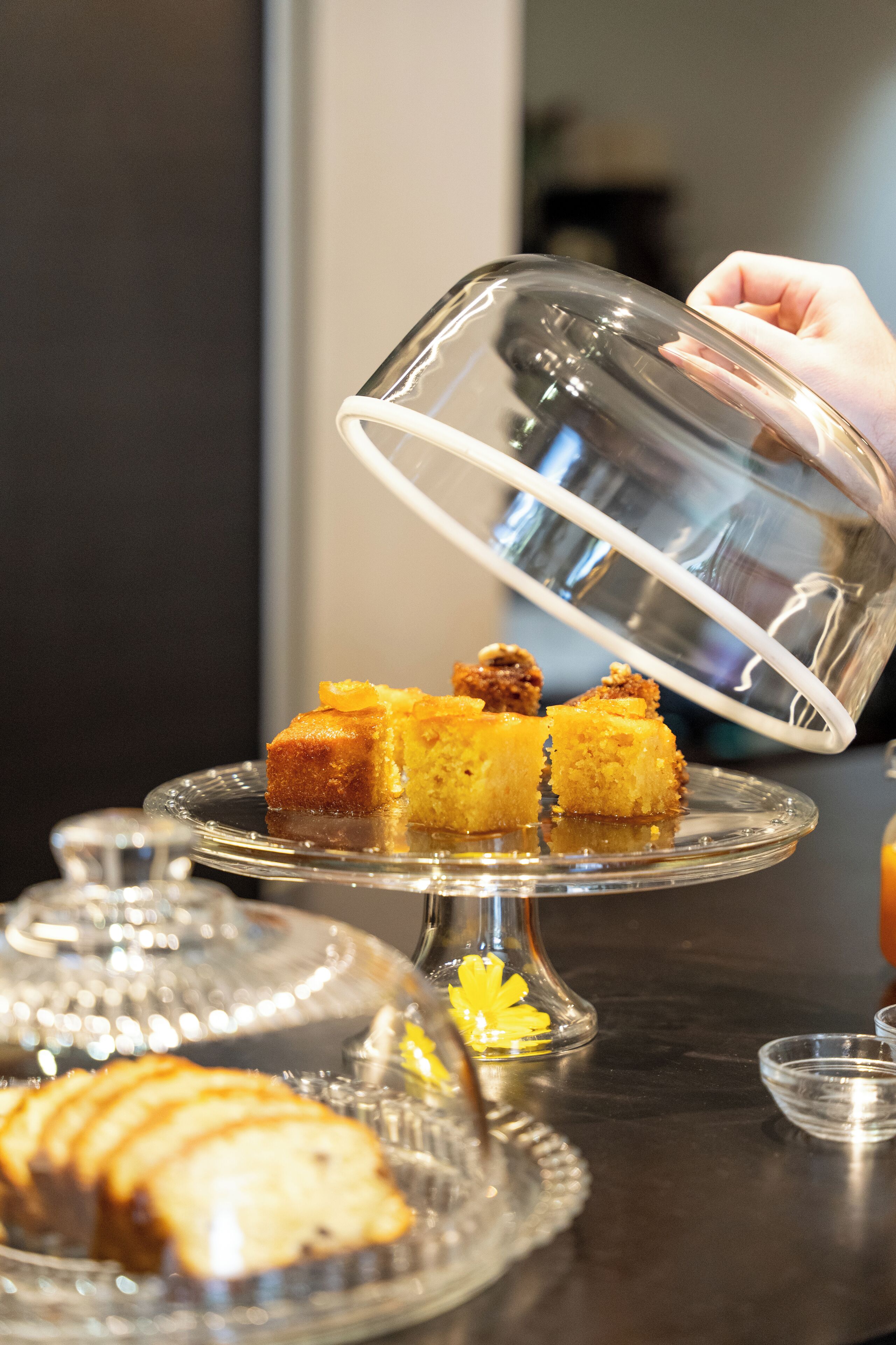A dessert display with a glass dome cover, a cake, and a slice being lifted.
