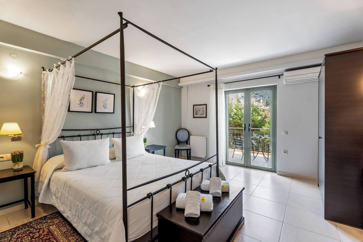 Una cama con dosel con sábanas blancas, una mesita de noche con lámpara y vistas al exterior a través de una puerta de cristal.