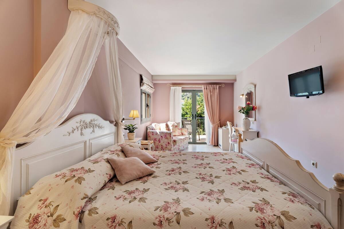 Un dormitorio con cama con dosel, televisión, balcón con vistas y una mesita de noche con lámpara.