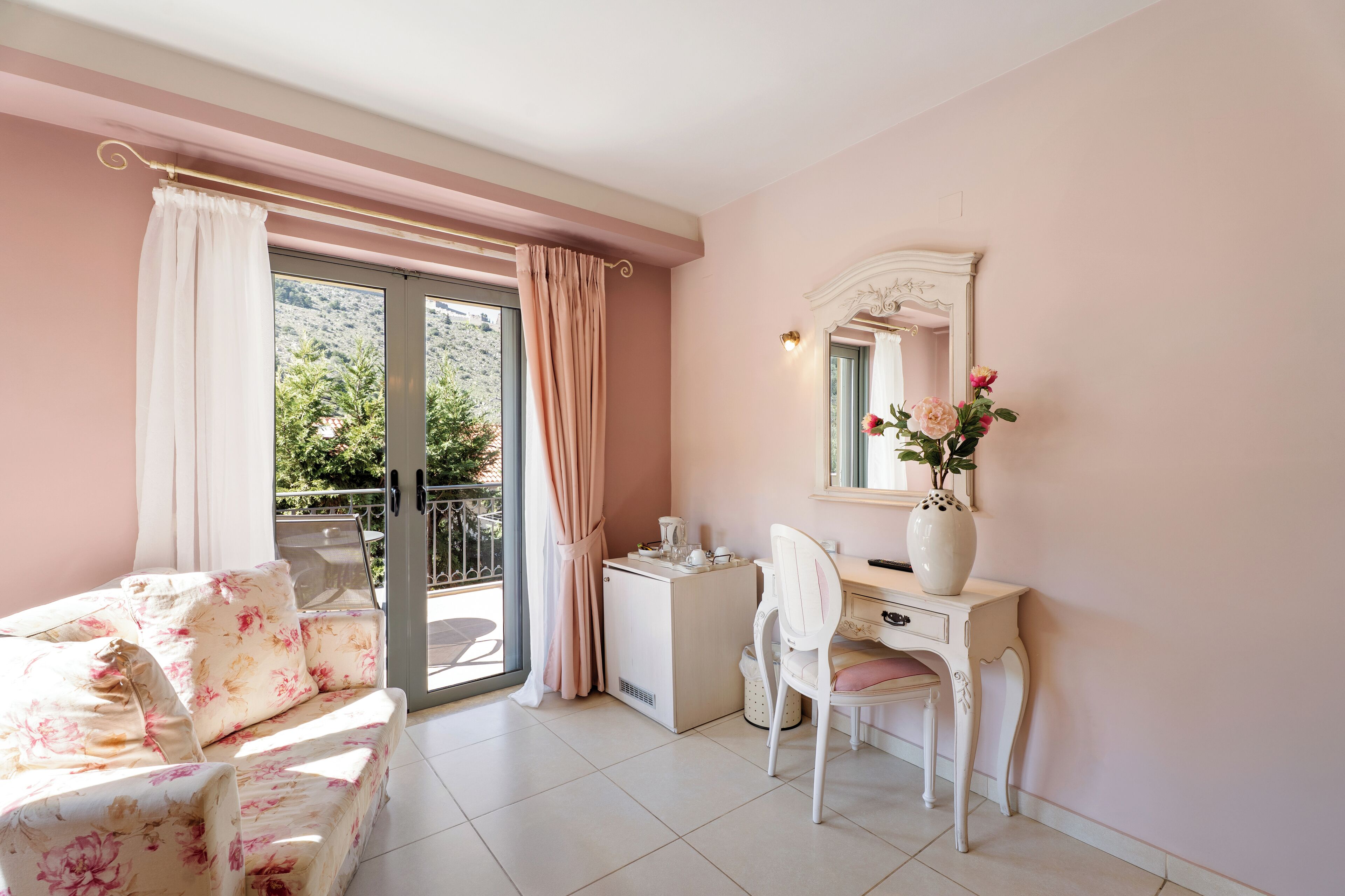 Una habitación con sofá, escritorio, silla, cómoda, espejo y ventana con cortinas.