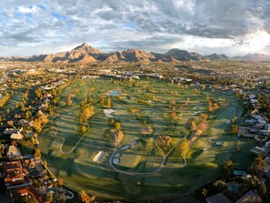 Un parcours de golf avec une chaîne de montagnes en arrière-plan, entouré de zones résidentielles.