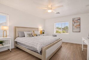 A bedroom with a bed, bedside tables, a ceiling fan, a window, and a wall-mounted artwork.