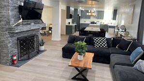 Ein modernes Wohnzimmer mit Kamin aus Stein, einer schwarzen Couch, einem Holztisch und einem Deckenventilator.