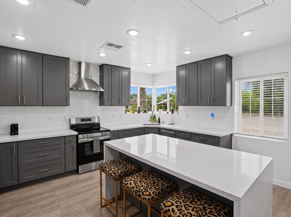 A modern kitchen with dark cabinets, a stainless steel range, and a large island with leopard print stools.