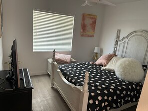 Une chambre à coucher comprenant un lit, un bureau, une chaise, une fenêtre avec des stores et un ventilateur de plafond.