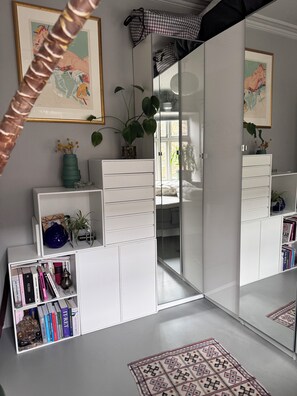 Quarto com guarda-roupa branco, estante, espelho e tapete estampado.