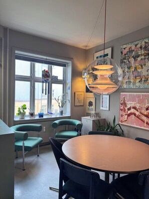 Uma sala de jantar moderna com uma mesa redonda, cadeiras cor turquesa, uma janela grande com vista e um lustre esférico pendente.