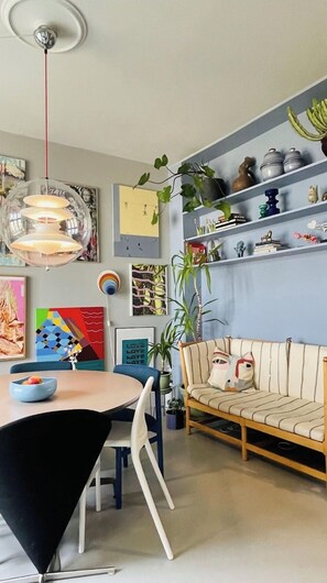 Una sala de estar moderna con una mesa redonda, sillas, un sofá, un ventilador de techo y estanterías empotradas con objetos decorativos.